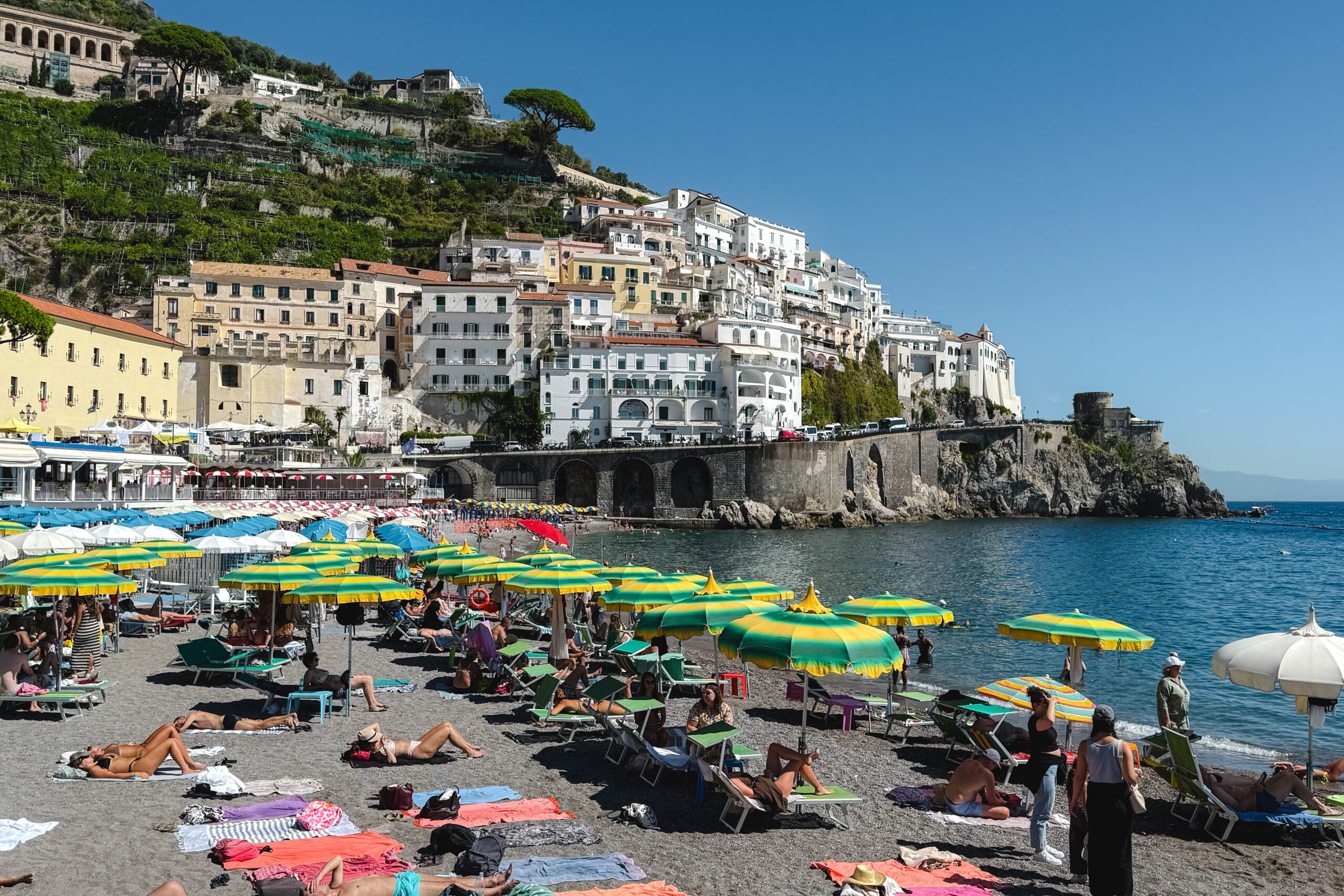 Colorful beach umbrellas and cliffside buildings along the Amalfi Coast waterfront in Italy.