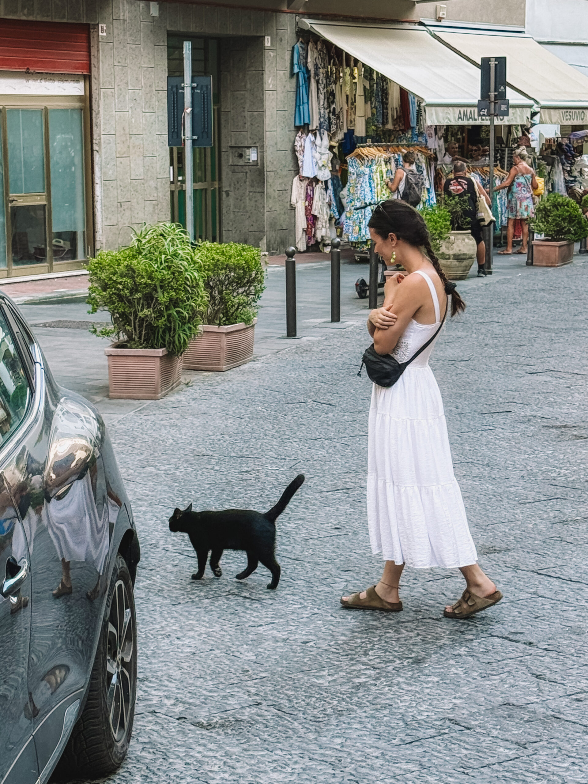 Woman walking past a black cat on a quiet Amalfi Coast street