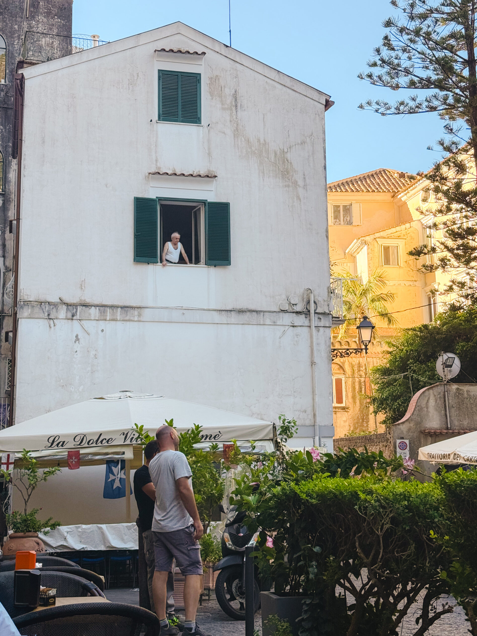Quiet morning street scene in Amalfi, Italy with a local man leaning out of a window above a café.
