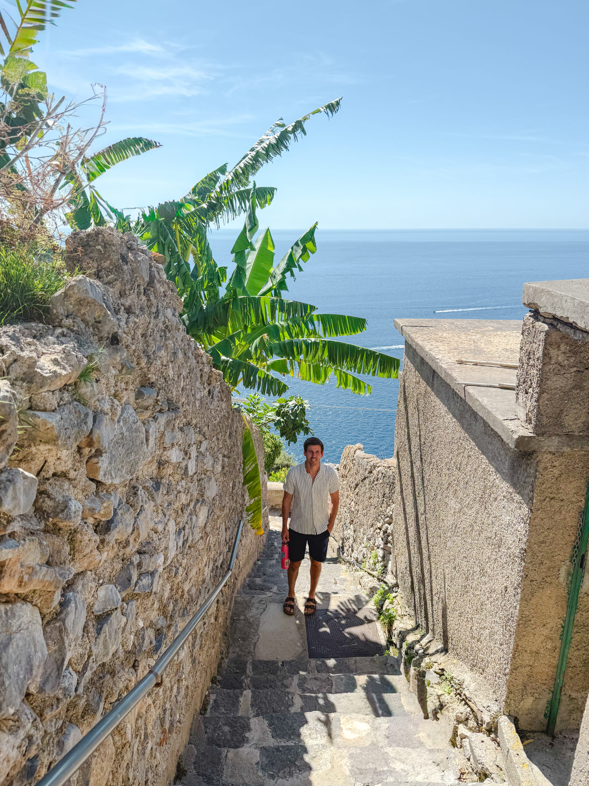 Man walking down a narrow stone staircase overlooking the sea in Conca dei Marini on the Amalfi Coast, Italy.